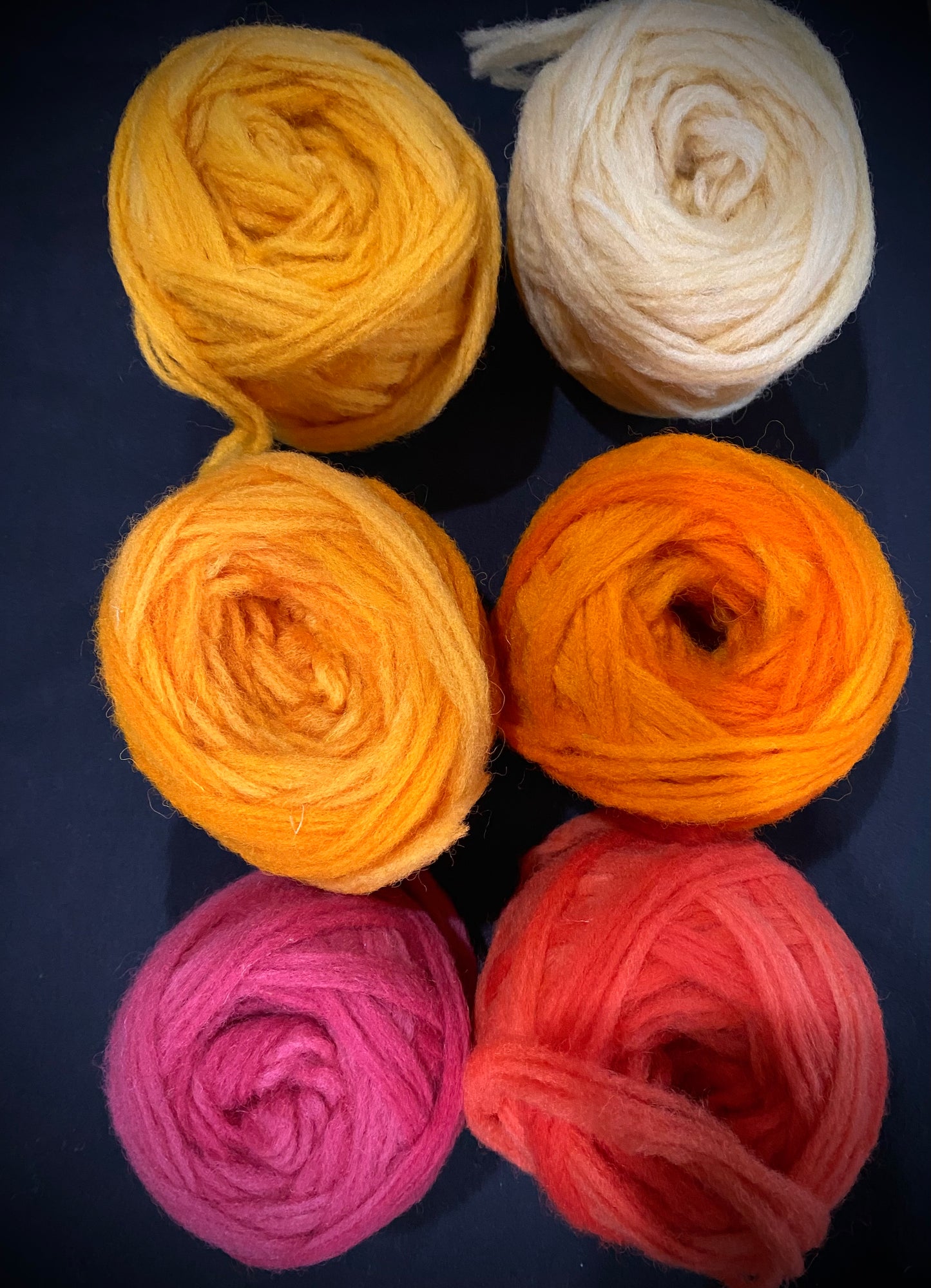 Six skeins of yarn in yellow, white, orange, pink, and red on a dark background